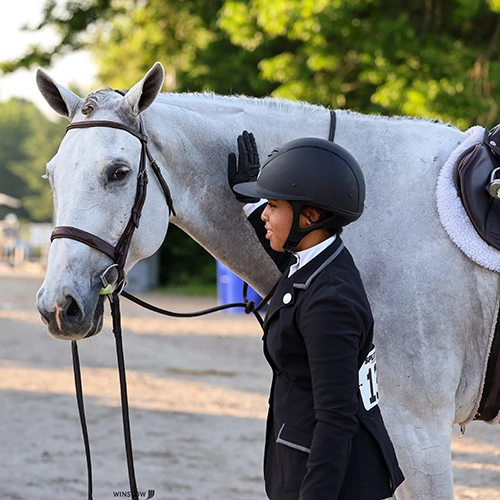 Savanna McMichael pets Latido, a gray horse, on his neck.